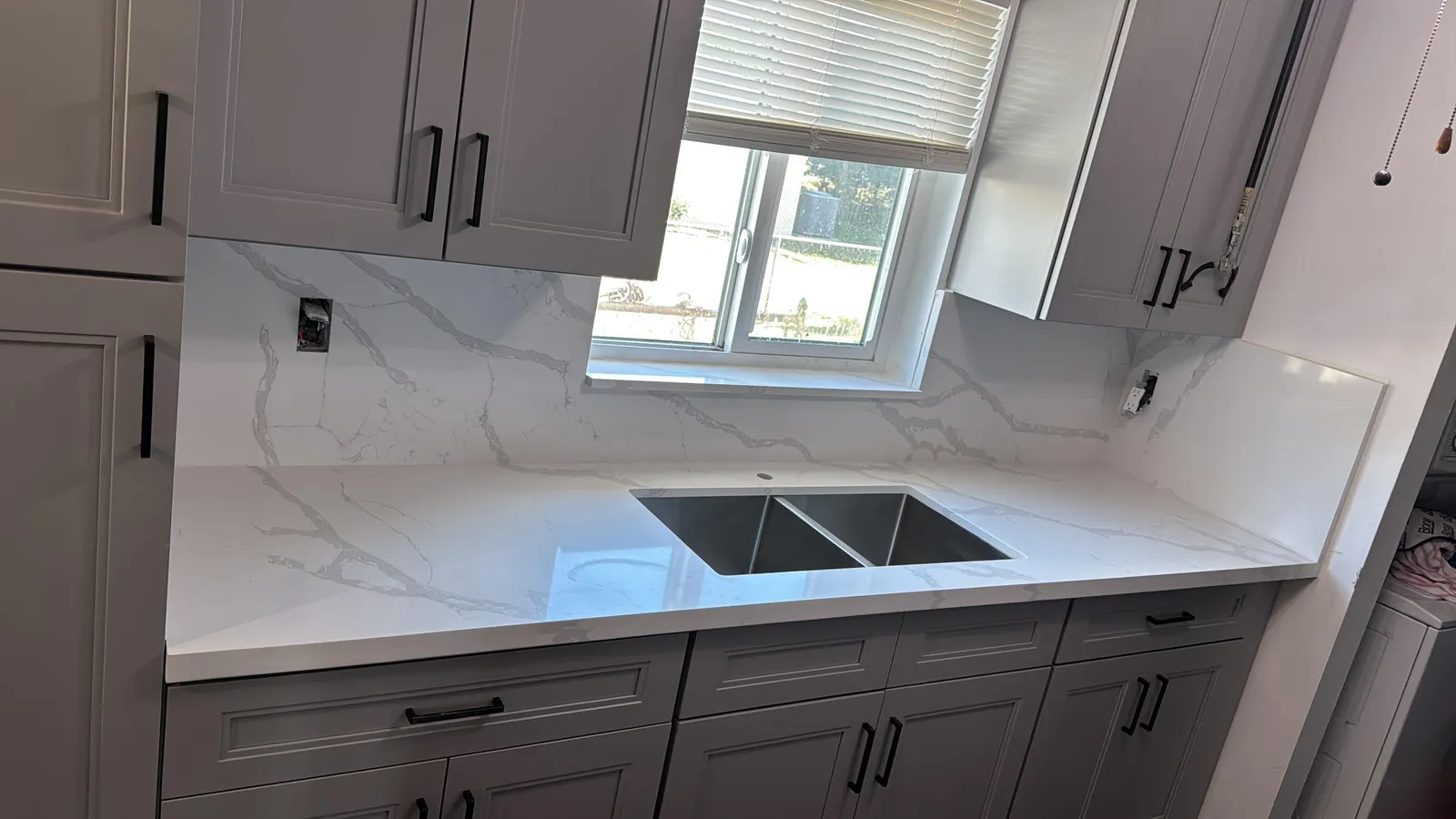 Remodeled kitchen with white quartz counters, marble-look backsplash and grey cabinets by MGS