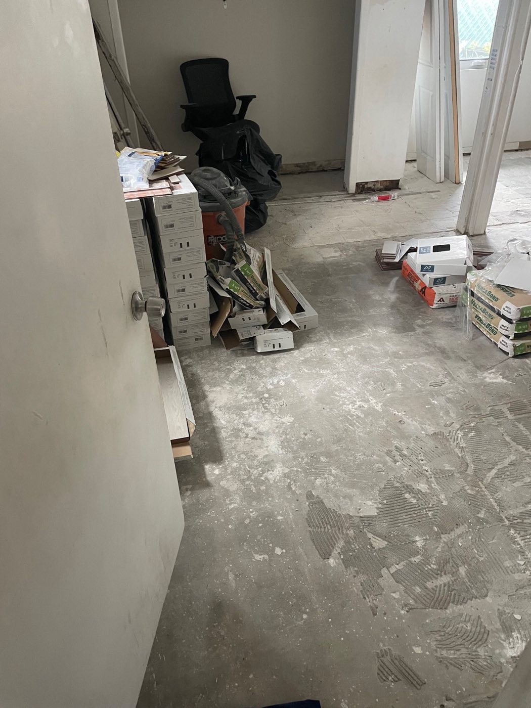 Room stripped to bare concrete slab, pipe stubs standing, tile stacked ready.