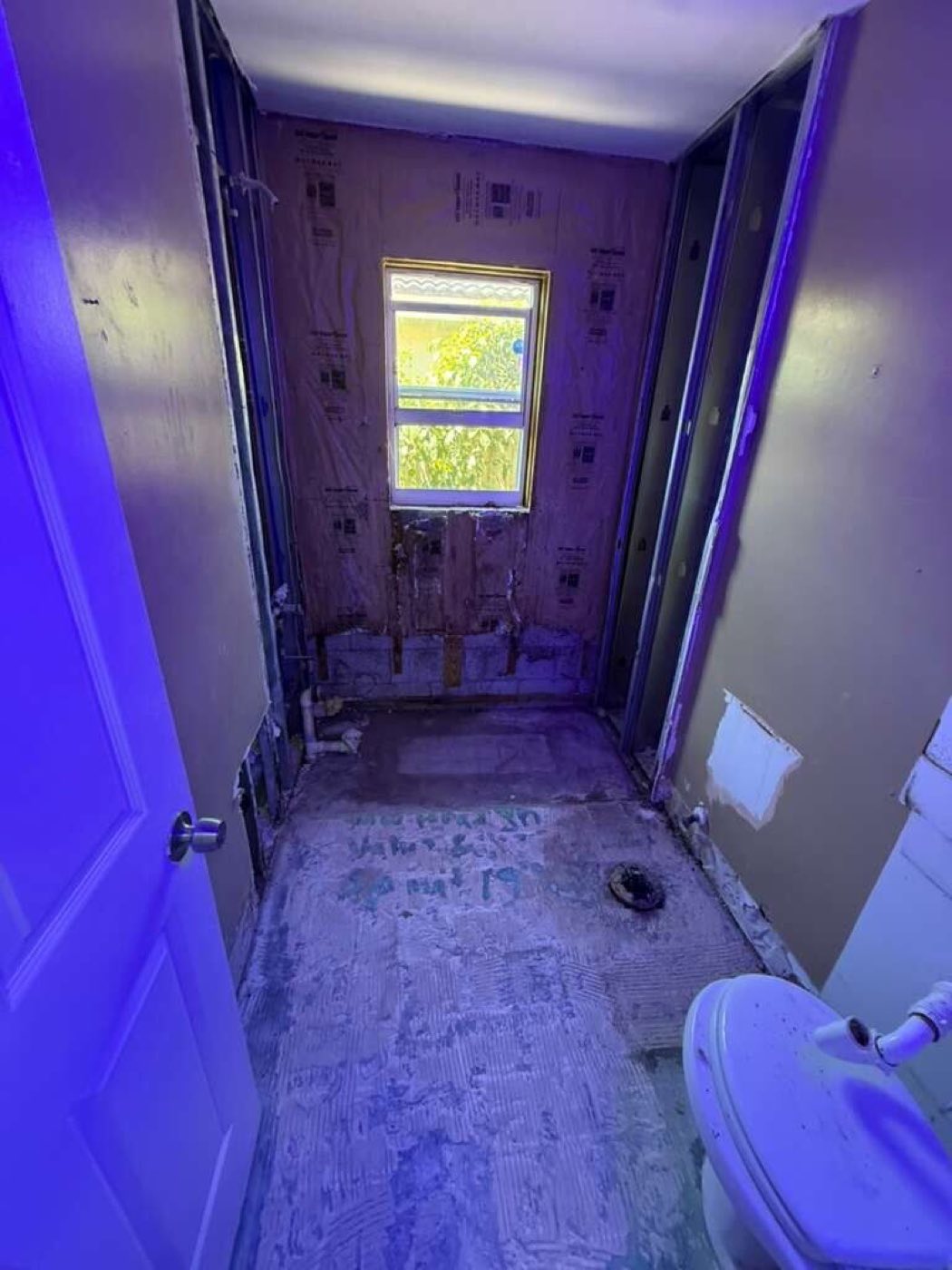 The bathroom stripped to the studs and slab, the window wall bare.