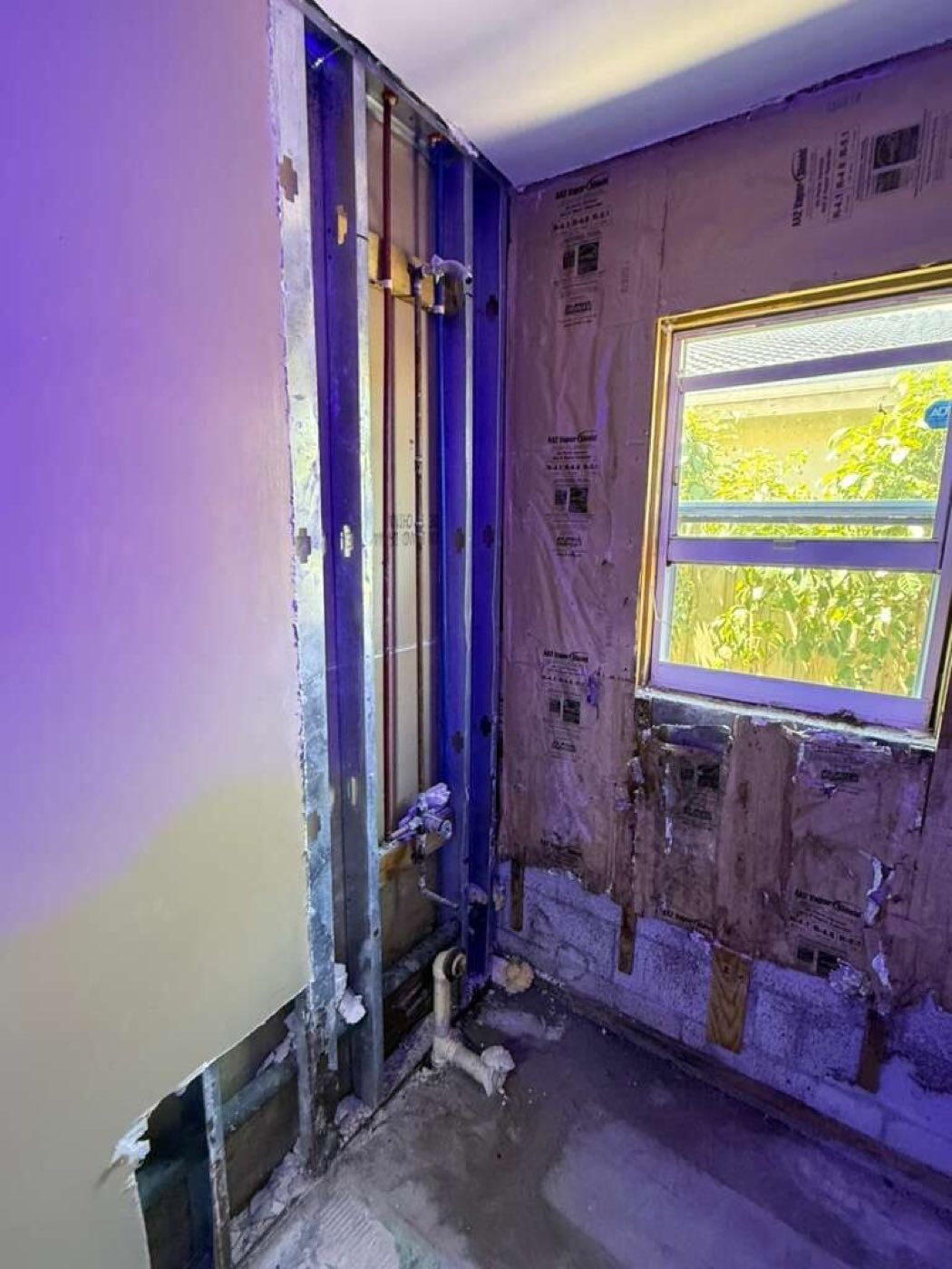 The tub wall opened, old plumbing exposed under the window.