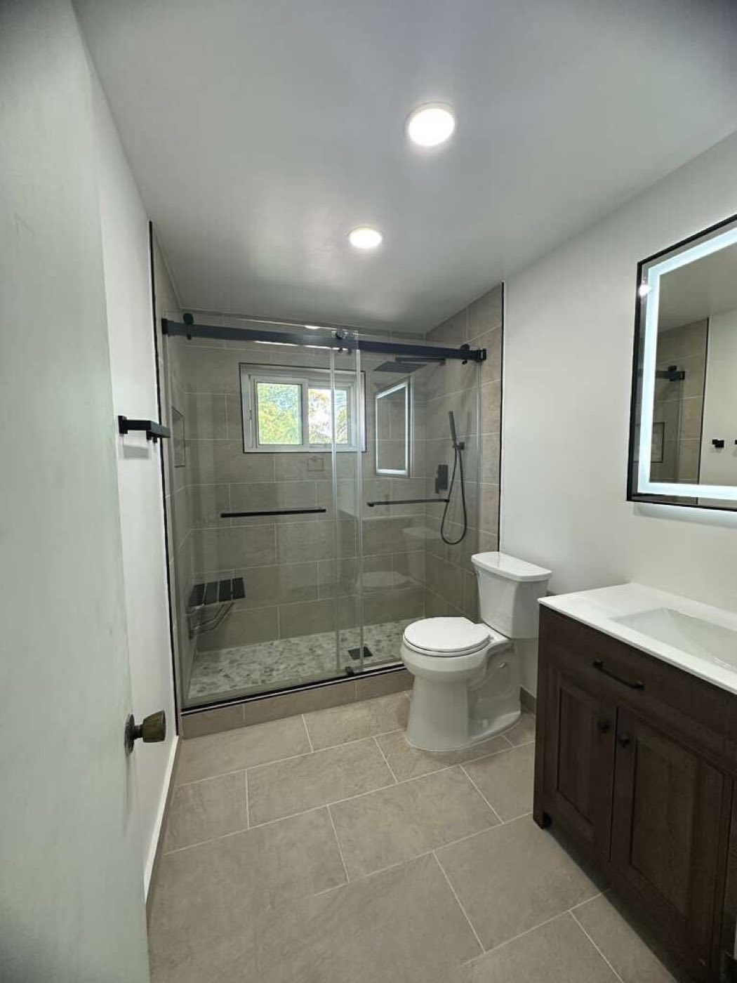 The finished bathroom from the door: glass shower, vanity and recessed lights.
