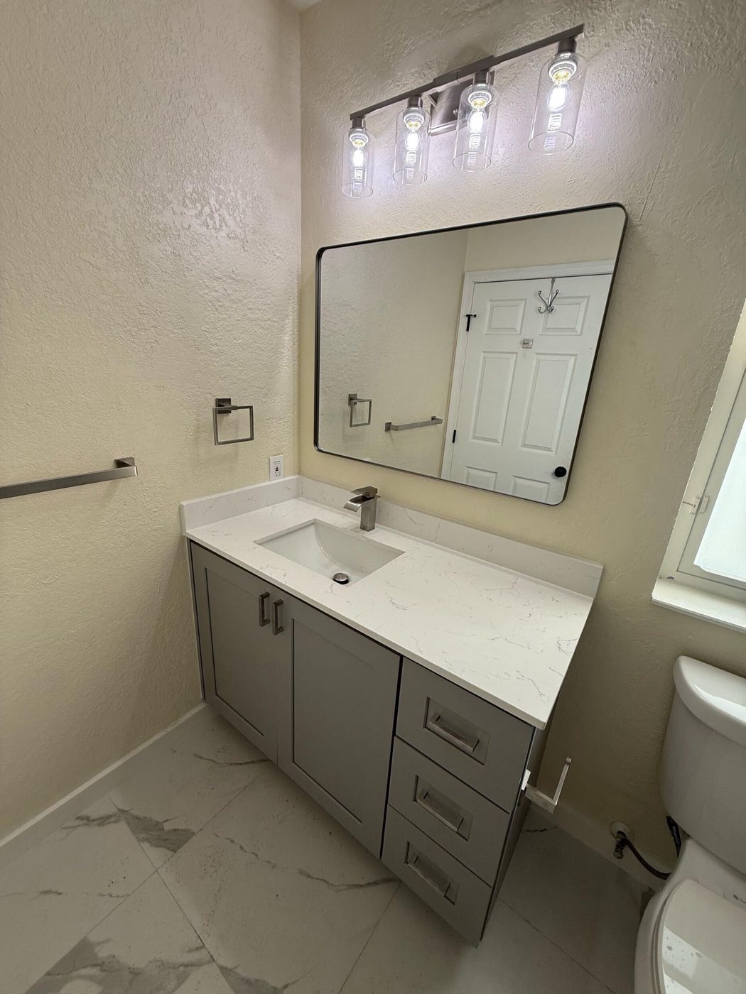 The finished vanity wall: grey cabinet, quartz top, black-framed mirror and light bar.
