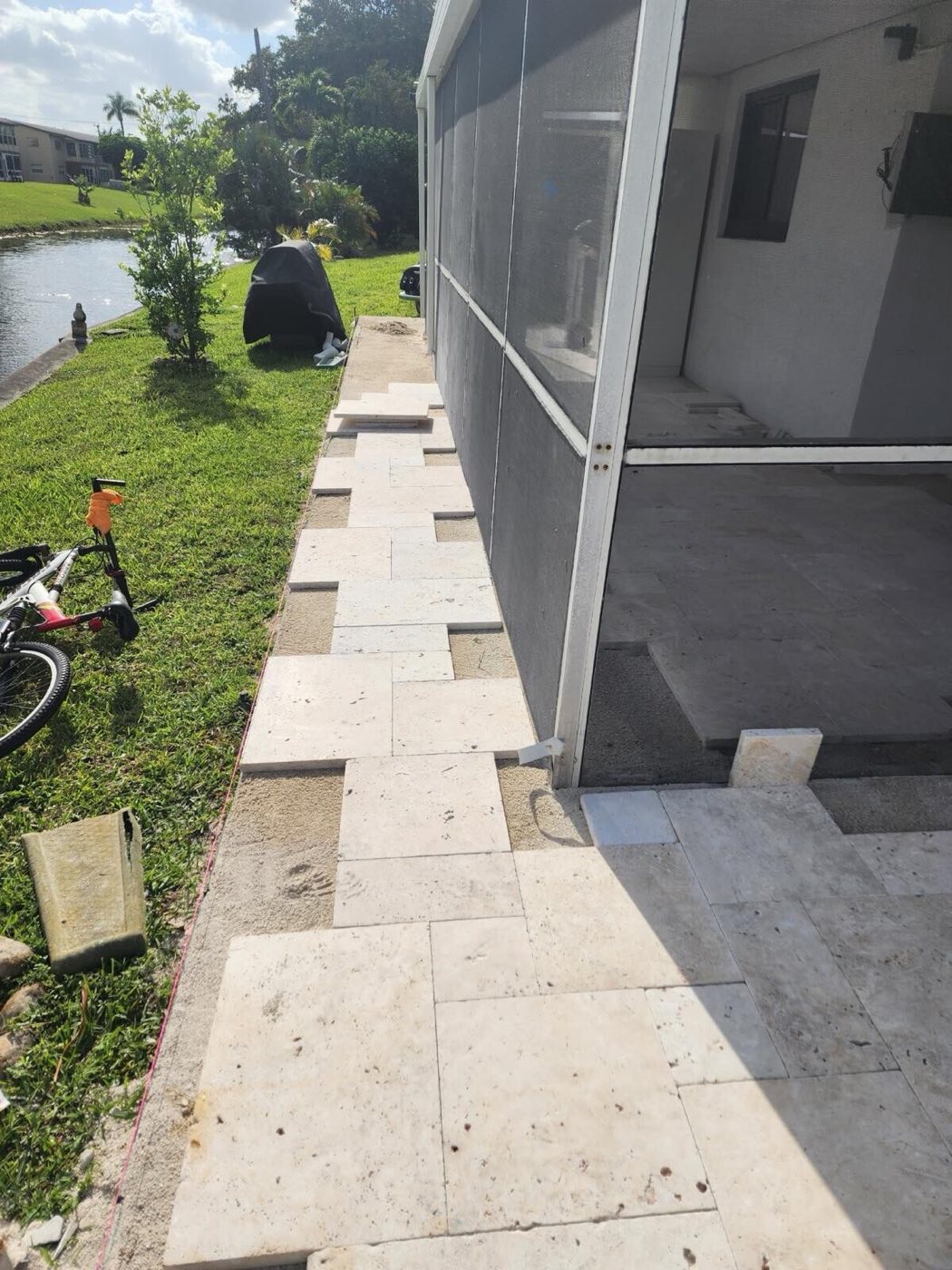 Travertine pavers being laid on a sand bed along the side of the screened lanai.