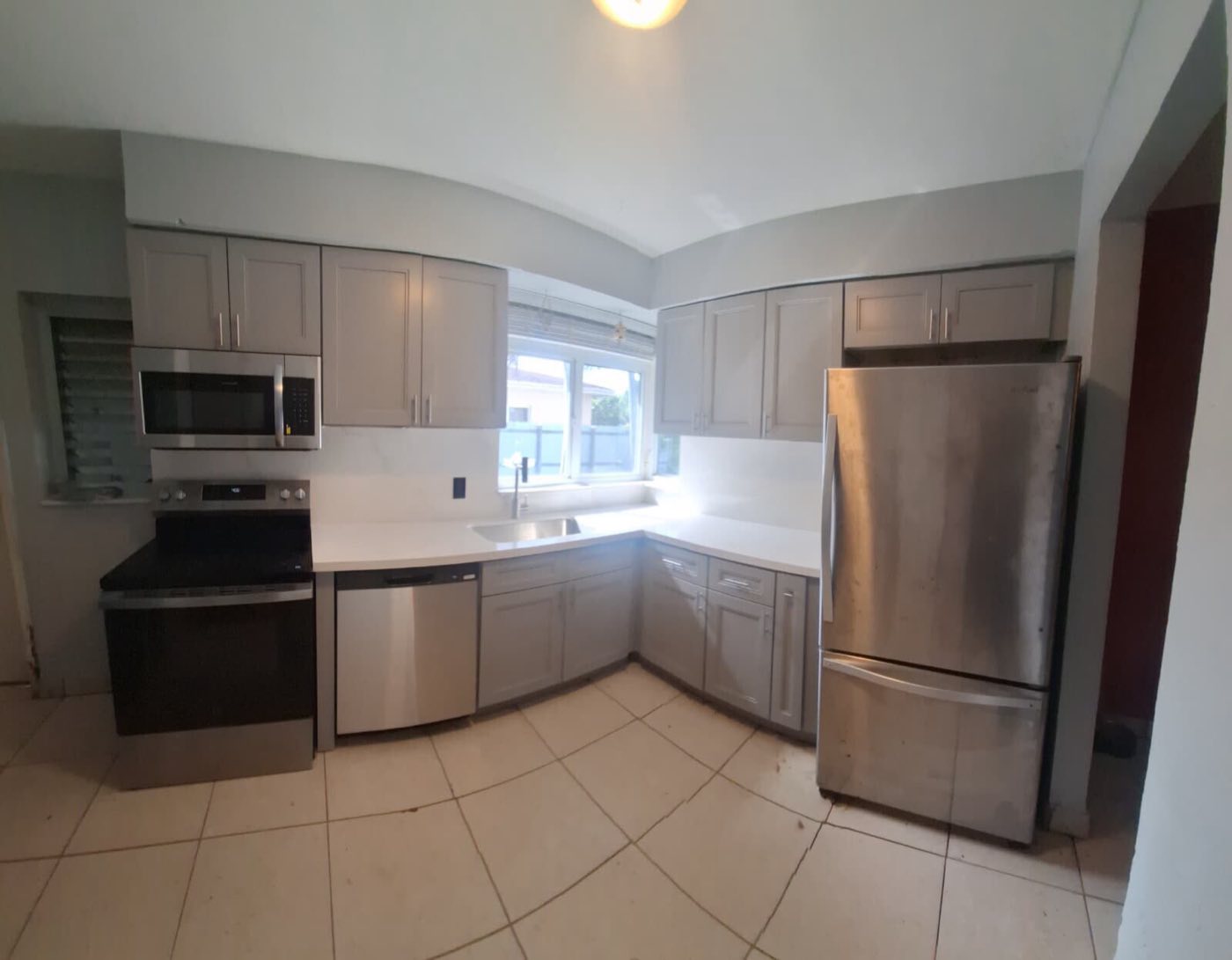 The finished kitchen: grey shaker cabinets, white counters, stainless refrigerator and range.