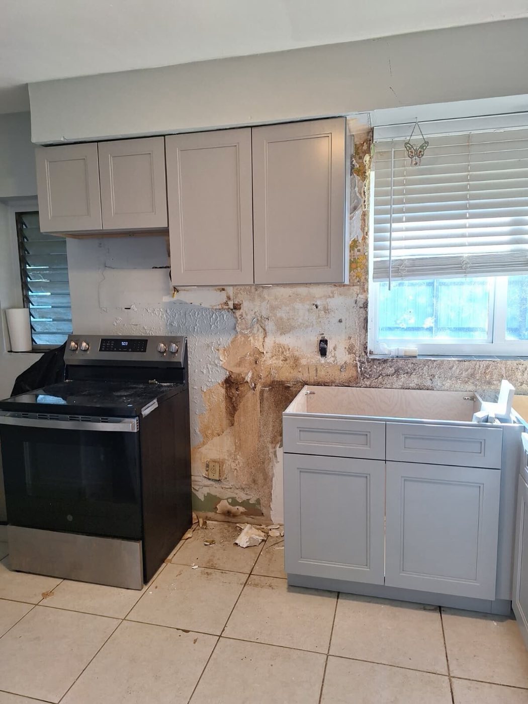 Grey shaker cabinets going in beside the opened wall, new range in place.